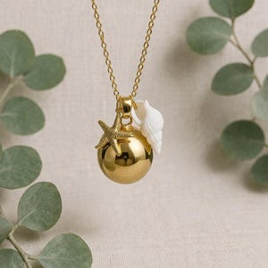 Peut inclure: Un collier doré avec un pendentif sphérique poli. Le pendentif est orné d'une breloque étoile de mer dorée texturée et d'un petit coquillage blanc en forme de spirale, le tout suspendu à une fine chaîne en métal doré.