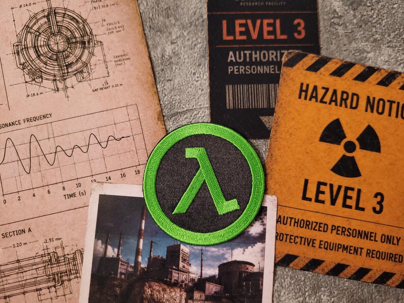 May include: A circular embroidered patch featuring a bright green Greek lambda symbol on a dark grey background. The patch is surrounded by technical blueprints, a photograph of an industrial facility, and a yellow hazard notice sign for Level 3.