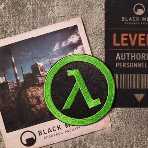 May include: A circular embroidered patch featuring a bright green lambda symbol on a black background with a green border. The patch is displayed alongside a photograph of an industrial facility and a Black Mesa Level 3 authorised personnel card.