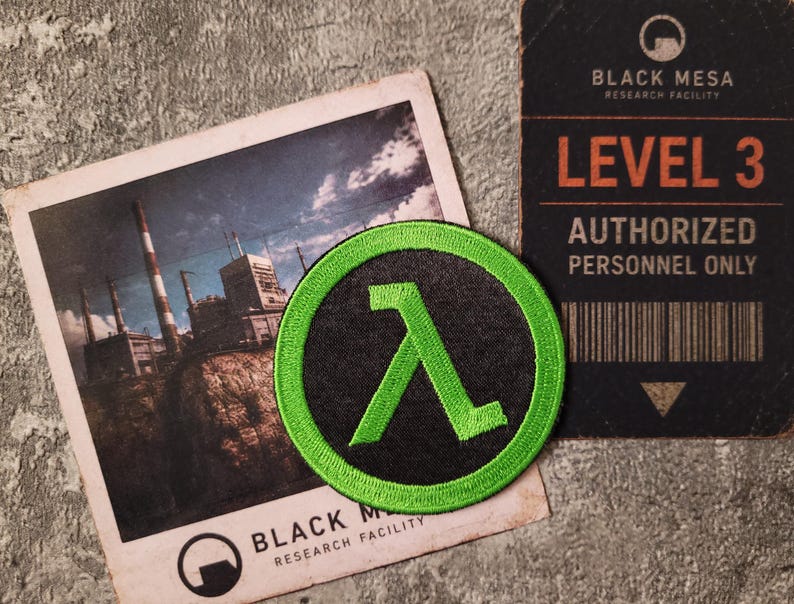 May include: A circular embroidered patch featuring a bright green lambda symbol on a black background with a green border. The patch is displayed alongside a photograph of an industrial facility and a Black Mesa Level 3 authorised personnel card.