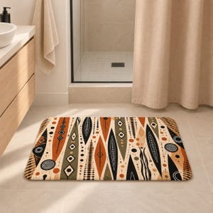 Op de afbeelding: Een rechthoekige badmat met een mid-century modern patroon van langwerpige ruitvormen, cirkels en abstracte lijnen in een kleurenpalet van gebrand oranje, olijfgroen, zwart en crème, gerangschikt in een herhalend verticaal ontwerp.