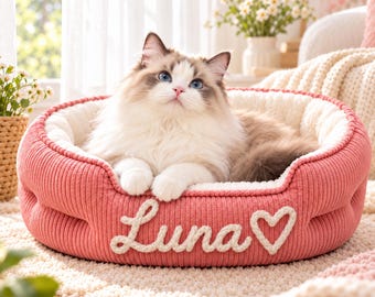 May include: A round, pink corduroy pet bed with a soft, cream-colored interior lining. The exterior features the name Luna embroidered in white script lettering, accompanied by a white embroidered heart symbol.