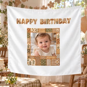 May include: A white fabric banner featuring the text HAPPY BIRTHDAY in brown and tan patterned letters. Below the text is a rectangular photo frame border made of patchwork squares in shades of green, brown, and white with floral and gingham prints.
