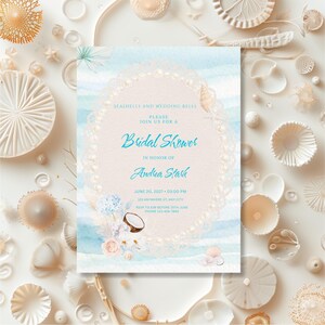 Puede incluir: Una tarjeta de invitación rectangular para despedida de soltera con fondo de acuarela azul claro, un marco ovalado central decorado con perlas blancas y detalles florales. El texto dice: Seashells and Wedding Bells, Please join us for a Bridal Shower in honor of Andrea Stark, June 20, 202X at 03:00 PM, 123 Anywhere St., Any City, RSVP to Kim before 10th June, Phone 123-456-7890.