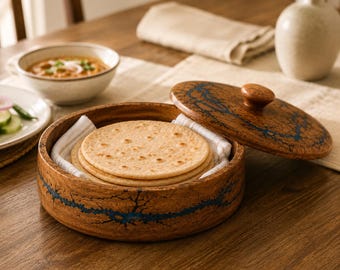 Puede incluir: Un recipiente redondo de madera con tapa, que presenta incrustaciones de resina azul oscuro con patrón de rayos. En su interior, una servilleta de tela blanca sostiene una pila de panes redondos, planos y de color marrón claro.