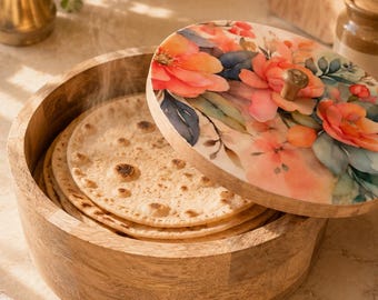 Puede incluir: Un recipiente redondo de madera con una tapa que presenta un estampado floral en tonos naranja, rosa y azul. El recipiente contiene varios discos de pan plano y tostado, con vapor visible saliendo del contenido caliente en su interior.