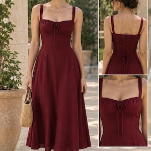 May include: A midi-length burgundy dress with a square neckline, thick shoulder straps, and a gathered bodice featuring a central tie detail. The back of the dress includes a corset-style lace-up closure with matching fabric ties.
