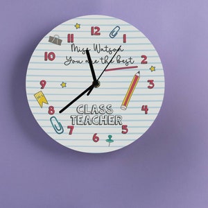 May include: A white clock with blue and red lines, a pencil, a paperclip, a pushpin, and a star. The clock face says "Class Teacher" and "Miss Watson You are the best".