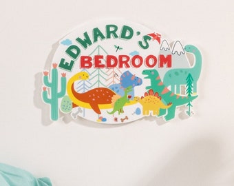 May include: A white oval-shaped sign with the text "Edward's Bedroom" in green and red letters. The sign is decorated with colorful dinosaurs, a cactus, and a mountain range.
