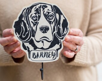 May include: A wooden dog head hook with a black and white illustration of a beagle. The hook is labeled "BARNEY" and has a metal hook.