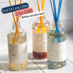 May include: Three clear glass reed diffuser bottles with labels reading Warm Cashmere, Fairy Dust, and Sleepy Lavender. The bottles contain liquid and botanical elements, with yellow reeds in two bottles and blue reeds in the third. Text overlays include End Of Line Offer, 3 for £20!, and While stocks last!.