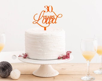 Może przedstawiać: Pomarańczowy akrylowy topper na tort z tekstem "30 Years Loved" w ozdobnym, pochylonym piśmie. Topper znajduje się na wierzchu białego, lukrowanego tortu.
