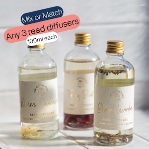 May include: Three clear glass reed diffuser bottles with gold screw caps, each containing 100ml of liquid and botanical elements. Labels feature the text The Gifting Knot, Warm Cashmere, Fairy Dust, and Sleepy Lavender. Text overlay reads Mix or Match Any 3 reed diffusers 100ml each.