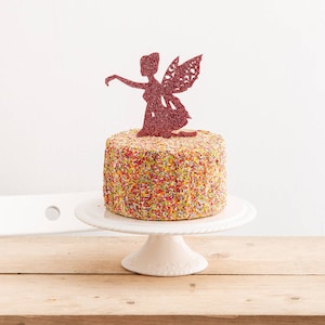 May include: A white cake decorated with colorful sprinkles and topped with a pink glitter fairy cake topper.