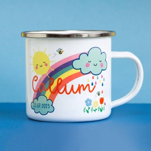 Puede incluir: Taza de esmalte blanco con un diseño de arcoíris, sol y nube. La taza está personalizada con el nombre "Callum" y la fecha "23.07.2023".