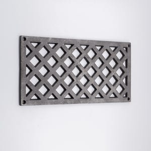 May include: A rectangular dark gray metal vent cover featuring a repeating diamond-shaped lattice pattern. The frame has four circular screw holes, one located in each corner, designed for secure mounting to a wall or floor surface.