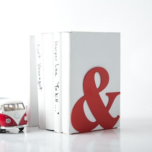 Peut inclure: Un serre-livres rouge et blanc en forme d'esperluette. Le serre-livres maintient trois livres. Le livre de droite a le titre "Harper Lee 'To Kill..." &eacute;crit sur le dos. Le livre de gauche a le titre "Kurt Vonnegut" &eacute;crit sur le dos.