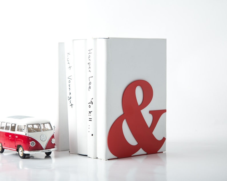Peut inclure: Un serre-livres rouge et blanc en forme d'esperluette. Le serre-livres maintient trois livres. Le livre de droite a le titre "Harper Lee 'To Kill..." &eacute;crit sur le dos. Le livre de gauche a le titre "Kurt Vonnegut" &eacute;crit sur le dos.