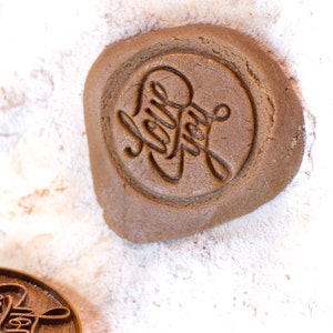 May include: A close-up of a brown cookie dough with the words "Holly Jolly" stamped into the dough. The dough is on a white surface covered in powdered sugar.