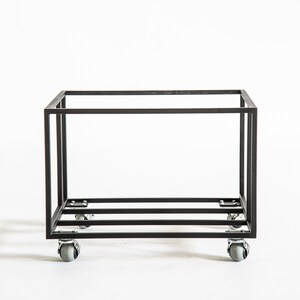 Minimalist black metal vinyl record storage cart with a clean rectangular frame and four rotating caster wheels, photographed against a white background.