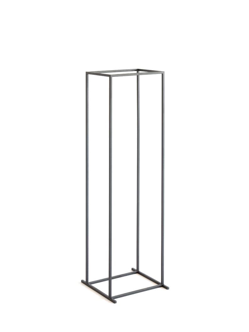 Slim tall black metal log rack with minimalist square frame, photographed on white background, modern Scandinavian indoor firewood holder design.