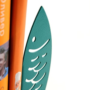 May include: Teal blue metal fish-shaped bookend with a cutout design. The bookend is holding up two books.