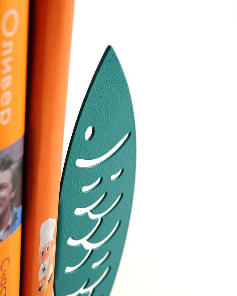May include: Teal blue metal fish-shaped bookend with a cutout design. The bookend is holding up two books.