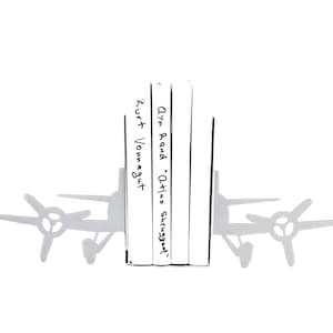 May include: A silver airplane bookend with the titles "Olyn Roud - Atlas Shrugged" and "Kurt Vonnegut" written on the books.