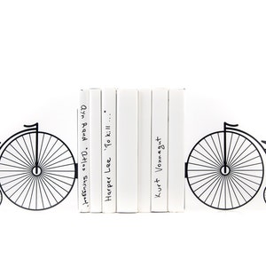 Black metal bookends Penny or Farthing Bike. The metal bike is on each side of the bookends. It is attached to the metal base with the side and the bottom, which holds the books vertically. The books press onto the bottom of the bookend.