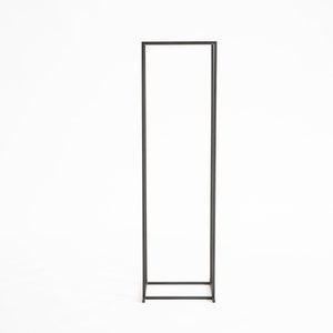 Tall minimalist black metal firewood rack frame standing on a white background, modern Scandinavian indoor log holder design.