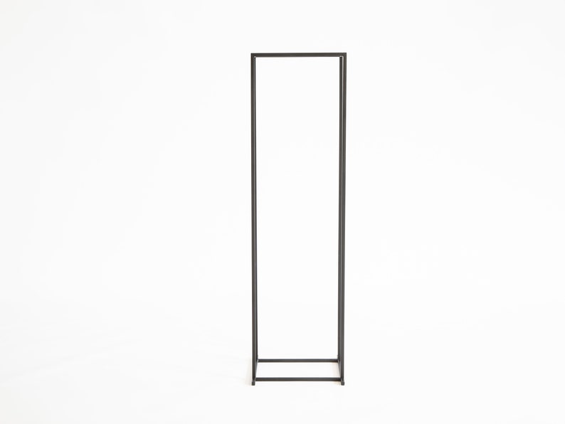 Tall minimalist black metal firewood rack frame standing on a white background, modern Scandinavian indoor log holder design.