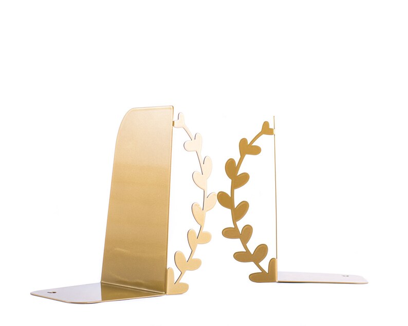 May include: Gold metal bookends with a leafy design. The bookends are shaped like a wreath with leaves and are a decorative way to hold books upright.