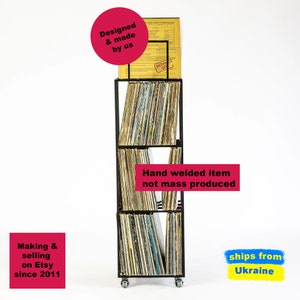 Front view of four-tier metal vinyl record stand on wheels, fully loaded with LP albums, minimalist square steel frame, hand-welded in Ukraine by Design Atelier Article on Etsy.