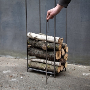 Person holding a fire poker, demonstrating modern minimalist Scandinavian log holder design for indoor or outdoor use.