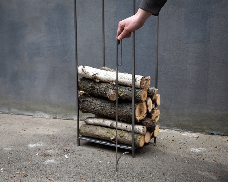 Person holding a fire poker, demonstrating modern minimalist Scandinavian log holder design for indoor or outdoor use.