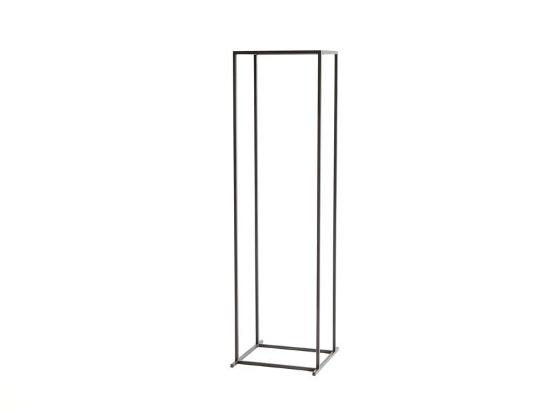 Angle view of a tall minimalist black metal log rack frame with four legs, showing modern Scandinavian firewood holder design.
