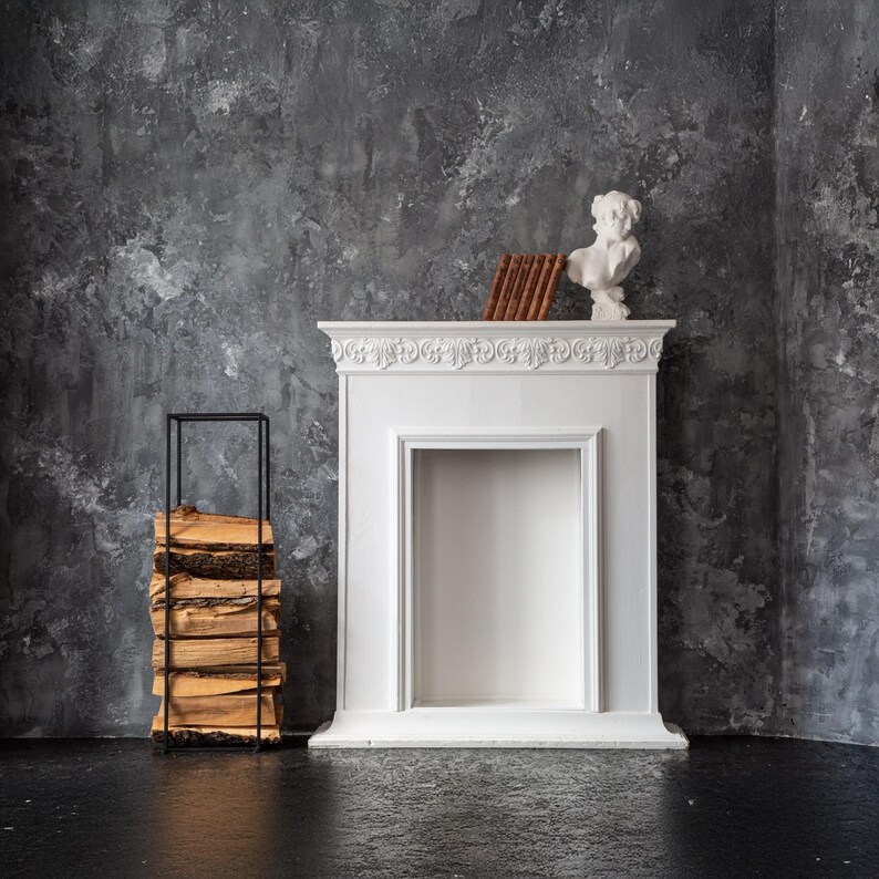 Modern black metal indoor firewood rack beside a white decorative fireplace with books and sculpture, styled in minimalist Scandinavian interior.