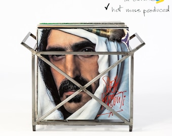 Puede incluir: Un estante para discos de metal plateado con una pila de discos de vinilo. El estante está soldado a mano y diseñado y fabricado en Ucrania. El texto "soldado a mano", "diseñado y fabricado en Ucrania", "producción en masa en caliente" y "Pedidos personalizados disponibles" está escrito sobre un fondo blanco.