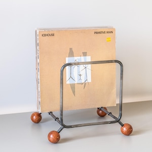 Könnte beinhalten: Ein Metall-Schallplattenhalter mit quadratischem Rahmen und Holzfüßen. Der Halter zeigt eine Stapel von Schallplatten, mit dem Albumcover von "Primitive Man" von ICEHOUSE sichtbar.