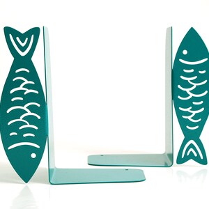 May include: A pair of teal blue metal bookends shaped like fish with white outlines. The fish have a simple design with scales and a fin.