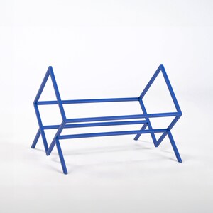 May include: A bright blue metal rack featuring a geometric frame with triangular side supports and a rectangular base. The structure is composed of thin, straight rods connected to form an open, angular storage unit with four legs.