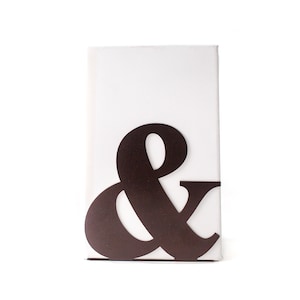 May include: A black metal bookend shaped like an ampersand symbol. The bookend is standing on a white surface.