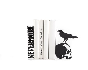 May include: Black metal bookends featuring a raven perched on a skull. The bookends are holding up three white books with the text "Harper Lee - To Kill..." written on one of the books. The left bookend has the word "NEVERMORE" written on it.