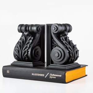 May include: A pair of black bookends with ornate scrollwork and leaf designs. The bookends are holding up a book with the title "Подземные ручьи" by М. КУЗМИН.