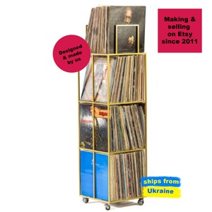 Angled view of yellow four-tier metal vinyl record stand on wheels, fully loaded with LP albums, minimalist square steel frame,