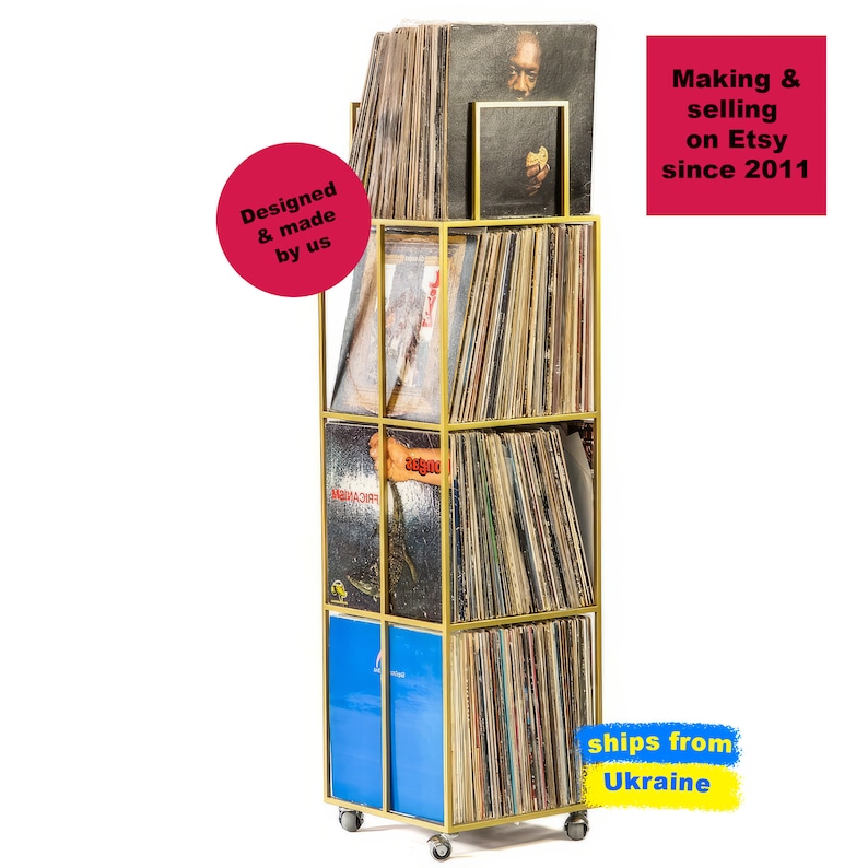 Angled view of yellow four-tier metal vinyl record stand on wheels, fully loaded with LP albums, minimalist square steel frame,