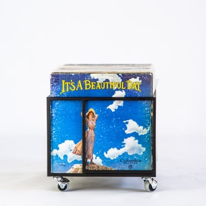 Front view of a black metal vinyl record cart on wheels, displaying the LP “It’s a Beautiful Day” in the front slot — minimalist industrial design for stylish vinyl record storage and display.