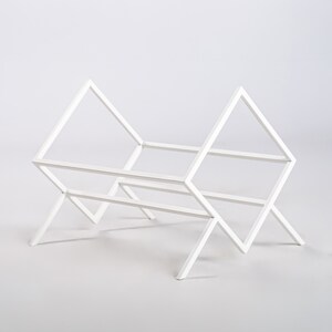 May include: A white metal rack featuring a geometric frame with two triangular side supports connected by horizontal bars. The structure is composed of thin, straight metal rods arranged in an open, angular design, providing a stable base.
