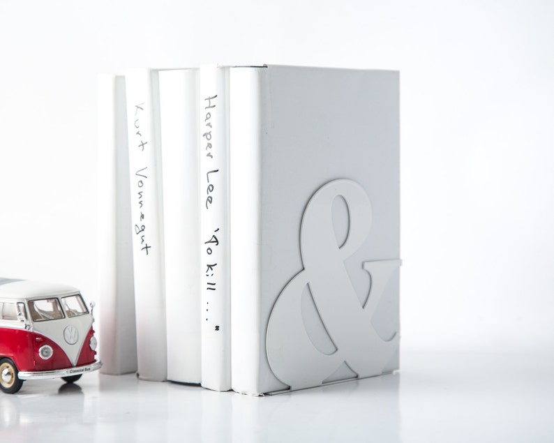 Peut inclure: Des serre-livres blancs avec un symbole ampersand sur le devant. Les serre-livres maintiennent trois livres blancs avec les titres "Kurt Vonnegut", "Harper Lee" et "To Kill..." &eacute;crits dessus.
