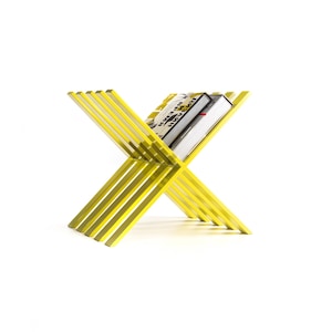 May include: A yellow metal magazine rack with a book resting on top. The rack is made of thin, straight metal bars that are crossed in an X shape.